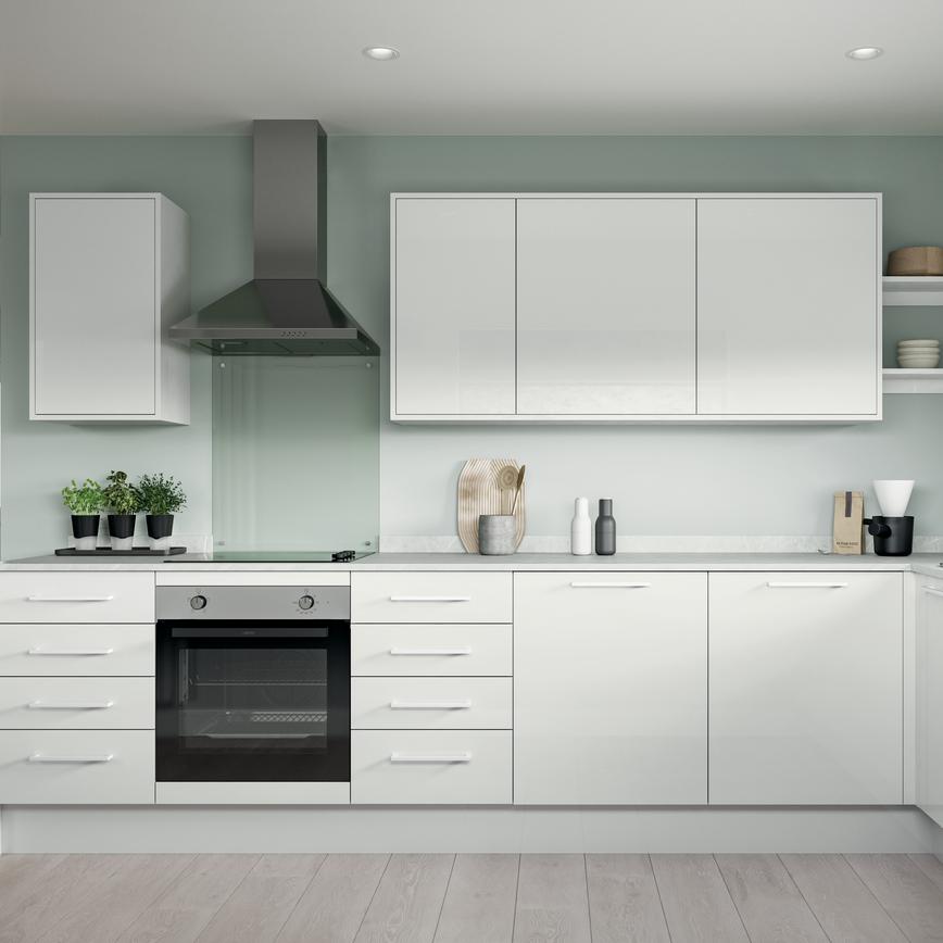 A small l-shaped kitchen using white slab doors in a glossy finish. Has white handles and worktops, and a built-under oven.