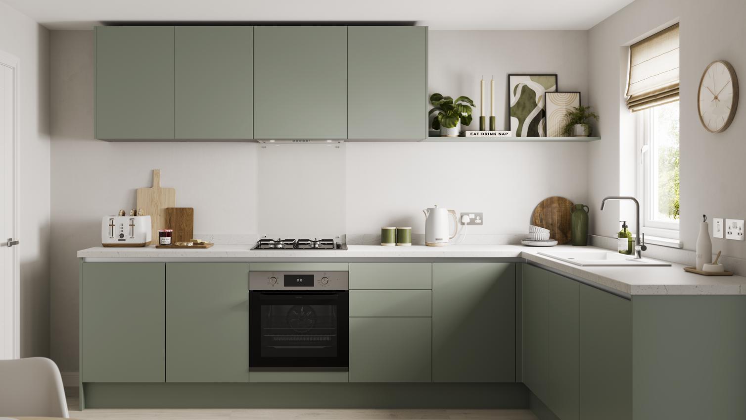 An l-shaped kitchen layout with green cabinets white marble-effect worktop, and pale wood flooring.