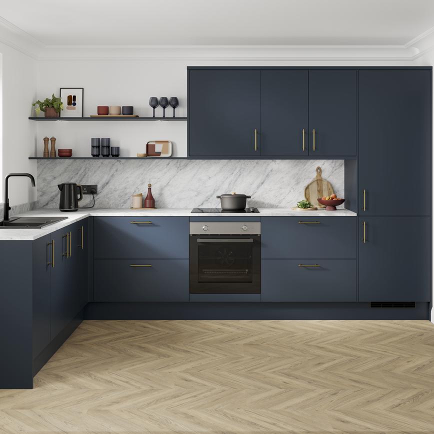 A marine blue kitchen with slab doors and brass handles. It is in an l-shaped layout, with grey worktop and oak flooring.