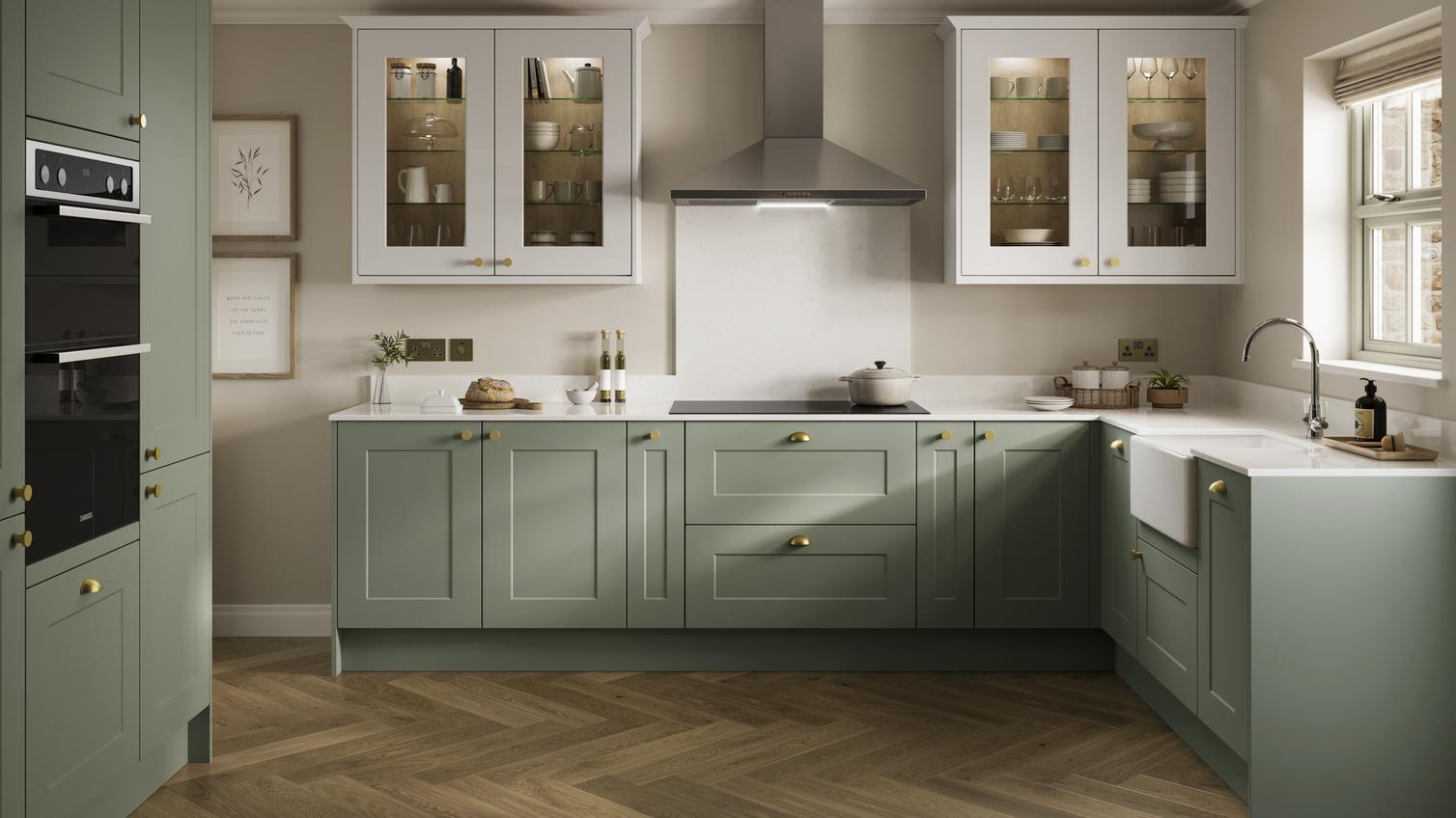 Light green shaker-style kitchen with glazed wall cabinets and herringbone oak flooring. Cabinets also have brass handles.