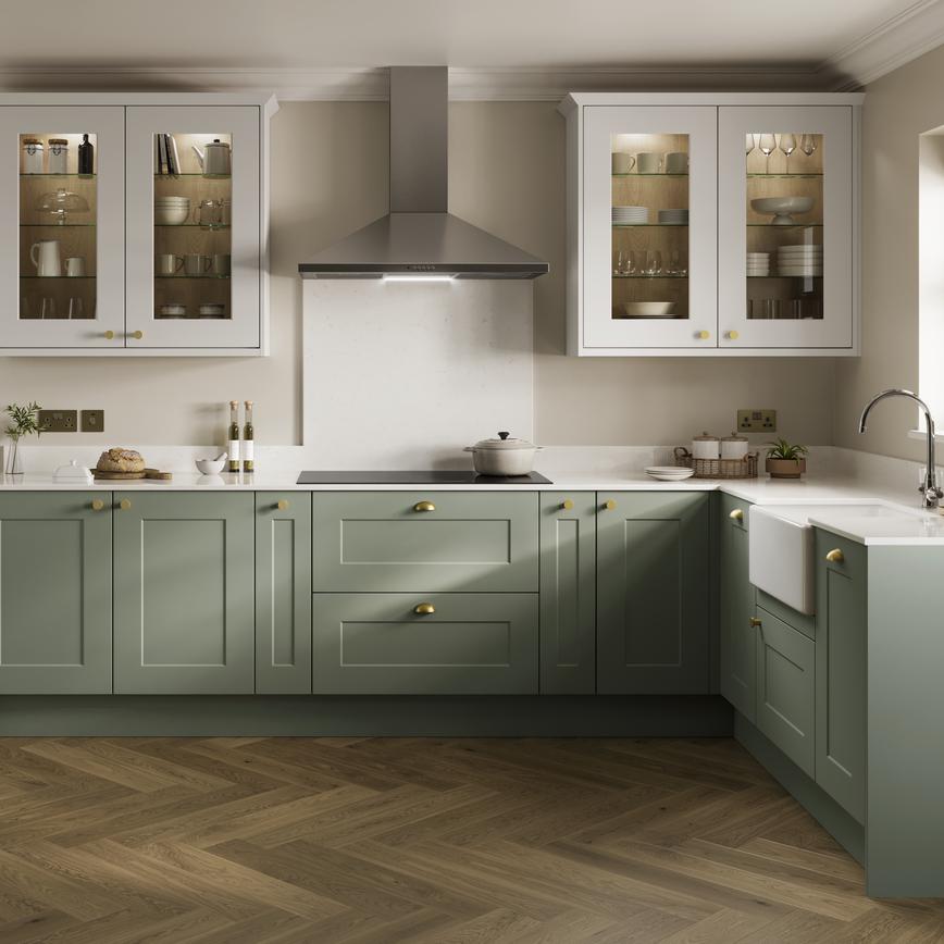 Light green shaker-style kitchen with glazed wall cabinets and herringbone oak flooring. Cabinets also have brass handles.