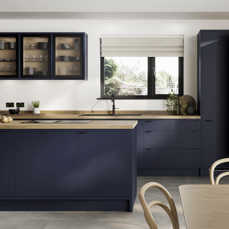 A contemporary blue kitchen with in-frame slab doors, white worktops, black handles, and glass units in an L-shape layout.