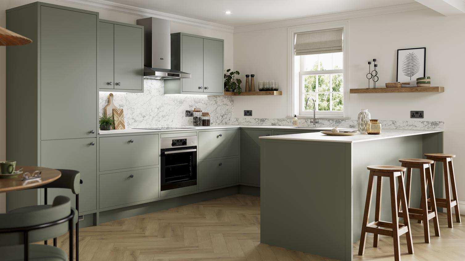 Green peninsula kitchen with matt finish and in-frame cabinet design. Features white counters and marble-effect splashback.