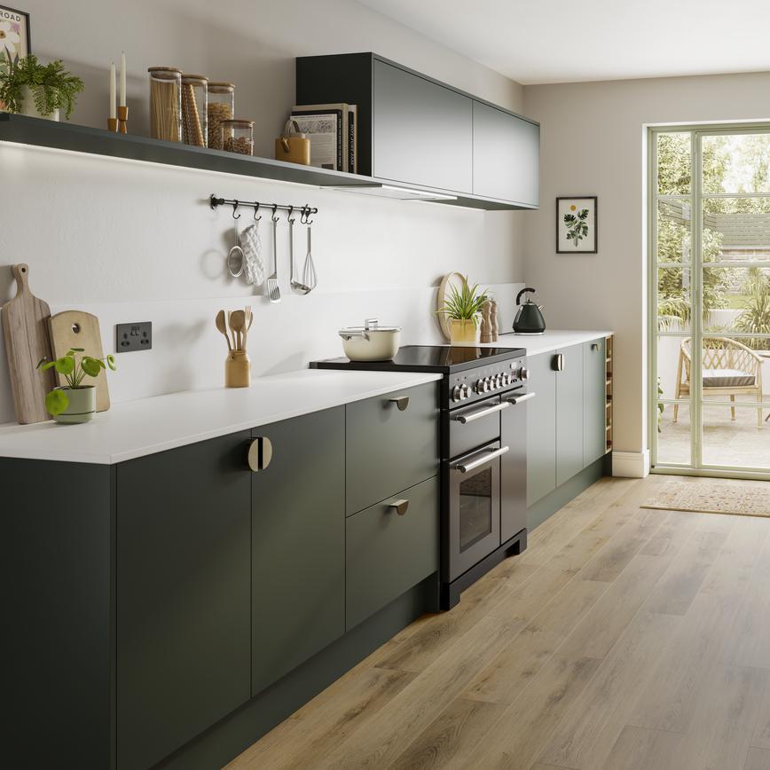 A dark green kitchen with matt cabinets, white countertops, range cooker, and warm oak-effect flooring.