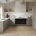 A sand grey, slab kitchen in a U-shaped layout. There are white worktops, plank flooring, and two large, black appliances.