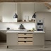 A sand grey, slab kichen with an L-shaped layout and in-frame design. It has white worktops and timber storage drawers.