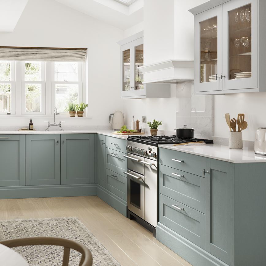 A blue kitchen idea with seafoam shaker cupboards. Contains white worktops, timber floors, and a double-bowl butler sink.
