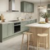 A shaker kitchen in a reed green colour, with wall units and larder cabinet. An oak-colour kitchen island is in the middle.