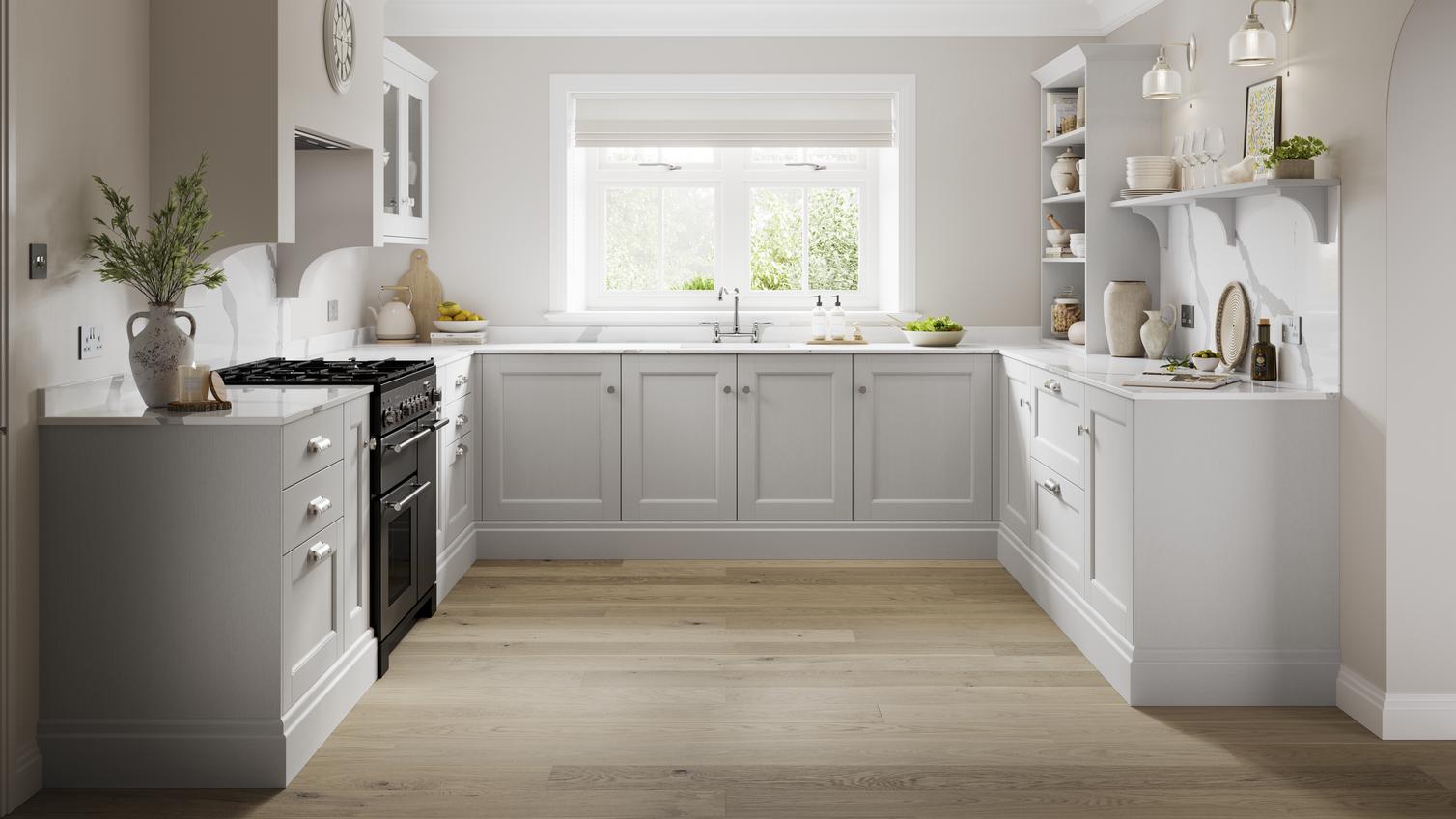 A dove grey shaker kitchen in a u-shape layout. It has oak-style flooring, white stone worktops, and a black range cooker.