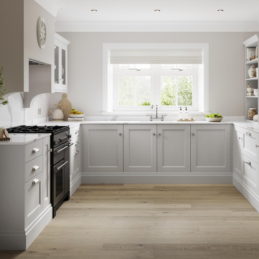 A dove grey shaker kitchen in a u-shape layout. It has oak-style flooring, white stone worktops, and a black range cooker.