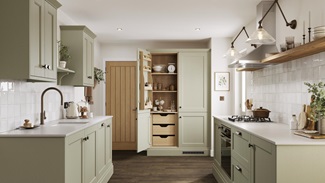 A sage green shaker kitchen with larder unit in a galley layout. It has dark oak flooring and shelving, and white worktops.