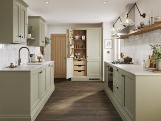 A sage green shaker kitchen with larder unit in a galley layout. It has dark oak flooring and shelving, and white worktops.