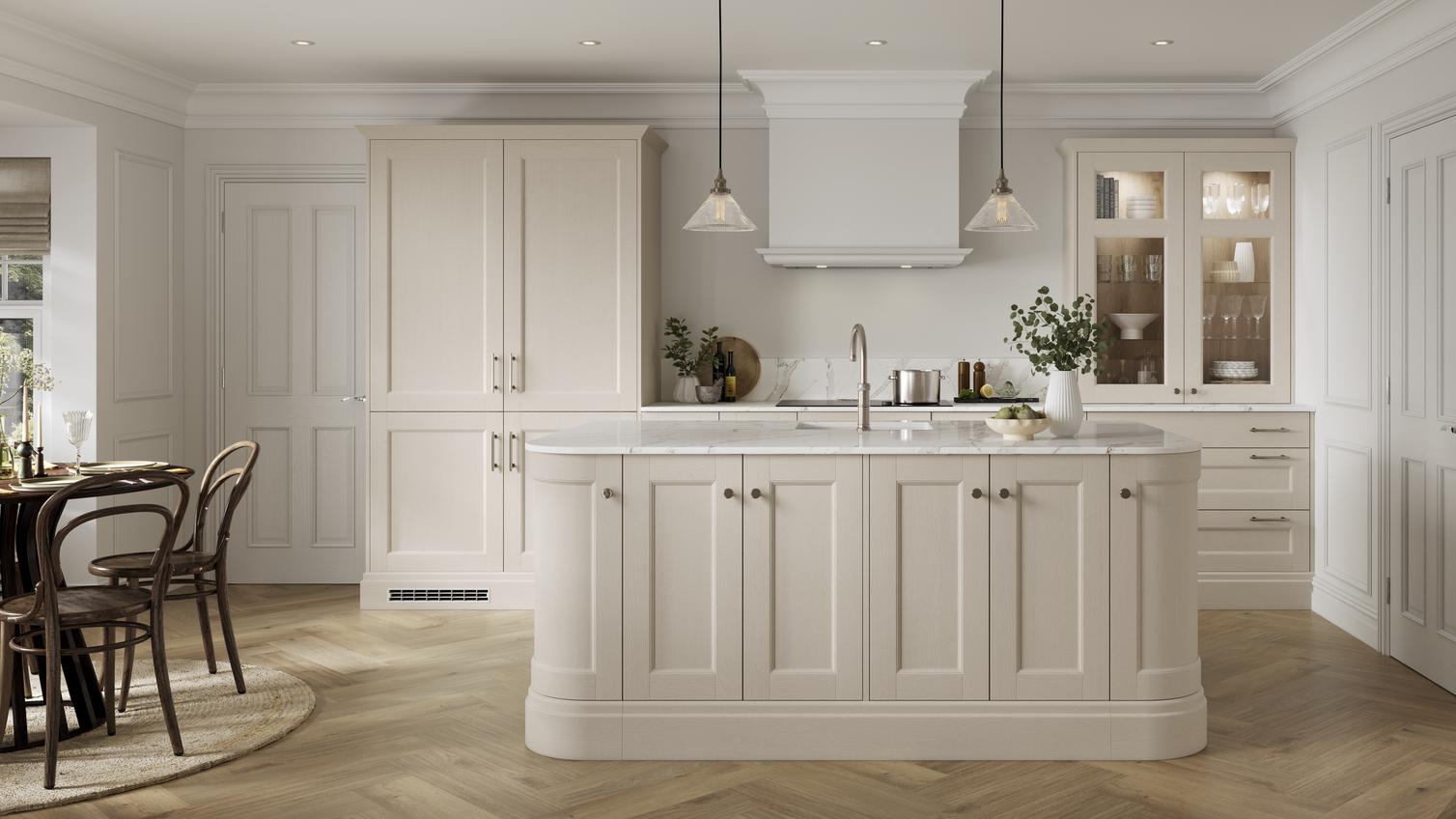 A cream, linen kitchen with shaker cabinets and glass doors. There is an island with curved corners and white worktop.