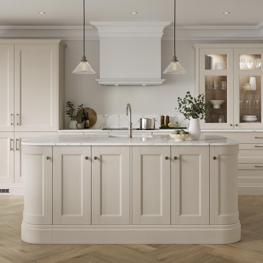 A cream, linen kitchen with shaker cabinets and glass doors. There is an island with curved corners and white worktop.