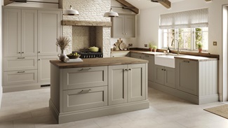 A sand grey, shaker kitchen in an L-shaped layout. There are timber worktops, pale plank flooring, and an undermount sink.