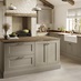 A sand grey, shaker kitchen in an L-shaped layout. There are timber worktops, pale plank flooring, and an undermount sink.
