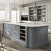 A blue shaker kitchen from Ilfracombe Dusk Blue, in an island layout with oak flooring. There is a run of linen-coloured cabinets