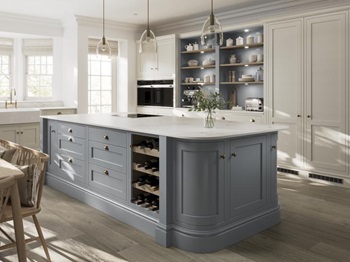 A blue shaker kitchen from Ilfracombe Dusk Blue, in an island layout with oak flooring. There is a run of linen-coloured cabinets
