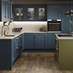 A marine blue shaker kitchen from Ilfracombe, in an l-shaped layout. It has an olive-colour island and oak plank flooring.
