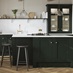 A green shaker kitchen from Ilfracombe Fir Green. It has a kitchen island, glass cabinets, and marble-style worktops.