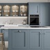 A laguna blue shaker kitchen from Ilfracombe, in an island layout with breakfast bar. It has white counters and stone floors