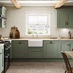 A reed green shaker kitchen from Ilfracombe, in an l-shaped layout. It has wall cabinets, stone flooring, and wood worktops.