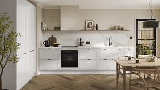 An l-shaped shaker kitchen, in a white colour. It has in-frame detailing with black handles and matching cabinet fixings.