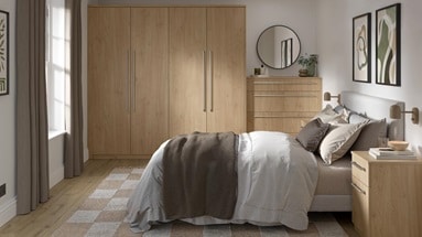 A bedroom with oak-fronted wardrobes, drawers, and dressers. The room has oak flooring and units have metallic rail handles.