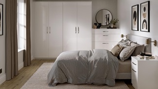A gloss white bedroom set, featuring metallic d-handles. There is oak plank flooring and matching bedside tables.