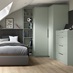 A reed green bedroom with a corner wardrobe and drawers. The room has a matching bedside table and oak-effect flooring.