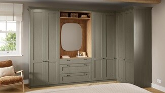 Shaker-style bedroom units in a pale, ash green colour. The tall cabinets feature a desser with drawers and rounded mirror.