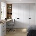 A bedroom with tall, gloss cabinets in a pale, dove grey finish. There is a desk with matching drawers and oak tabletop.