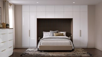 A bedroom with slab, white cabinets in a gloss finish. There is a drawer desser and tall units alongside and above a bed.