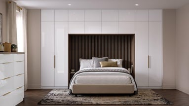 A bedroom with slab, white cabinets in a gloss finish. There is a drawer desser and tall units alongside and above a bed.