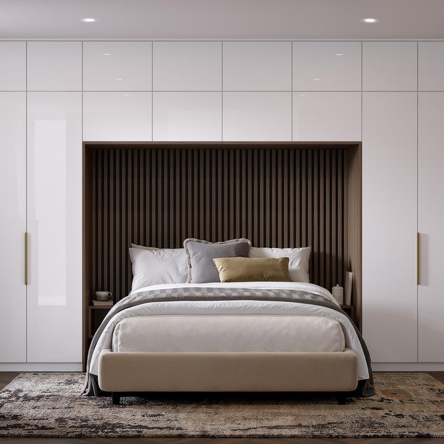 A bedroom with slab, white cabinets in a gloss finish. There is a drawer desser and tall units alongside and above a bed.