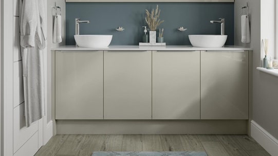 Small slab bathroom with gloss cupboard doors in sandstone. Has two white sinks, chrome handles and taps, plus a teal wall.