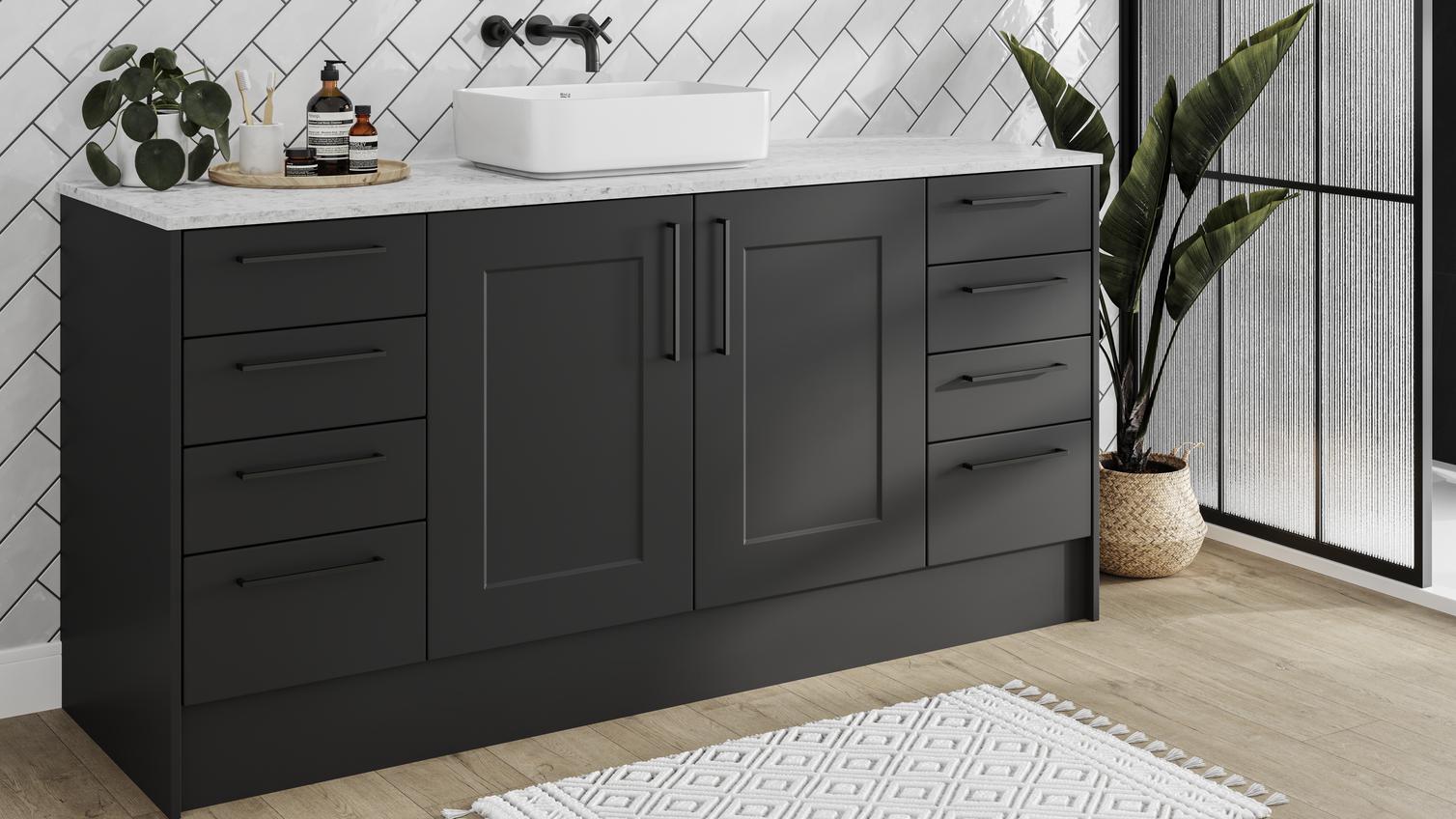 Black shaker cupboard doors in a compact bathroom. Has white metro tiles, a white worktop, a round mirror, and an oak floor.