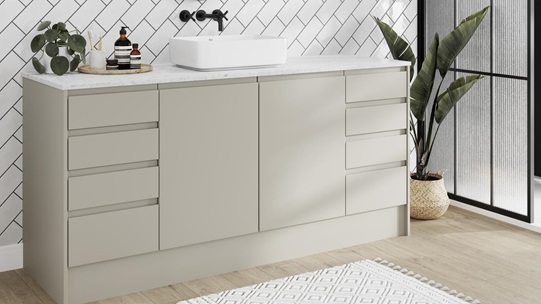 Modern integrated handle bathroom with matt sandstone cupboard doors, drawers, white worktop and tiles, and a black tap.