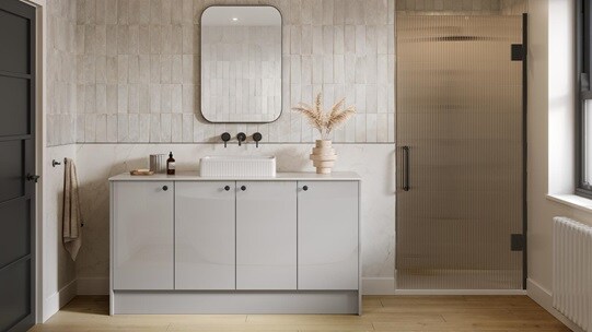 A gloss, dove grey bathroom with a single sink and black hardware. There is a glass shower door next to the vanity cabinets.
