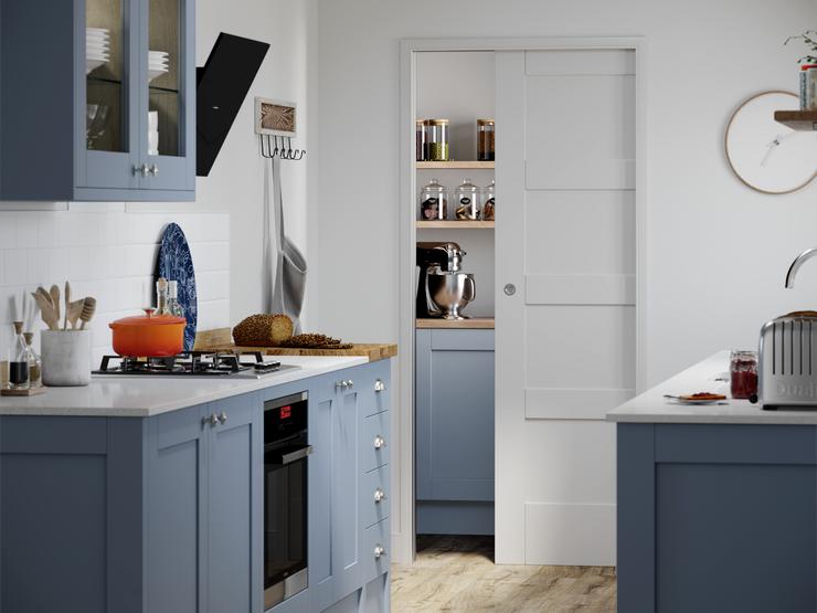 A white pocket door in a blue, shaker kitchen in a galley layout