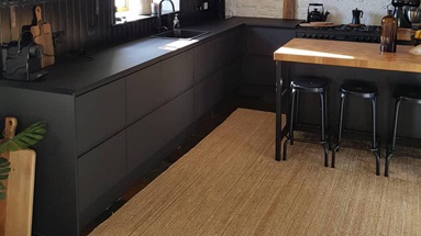 A rustic black kitchen idea with integrated handle doors and timber floors. Has a L-shaped layout and a black cooker hood.