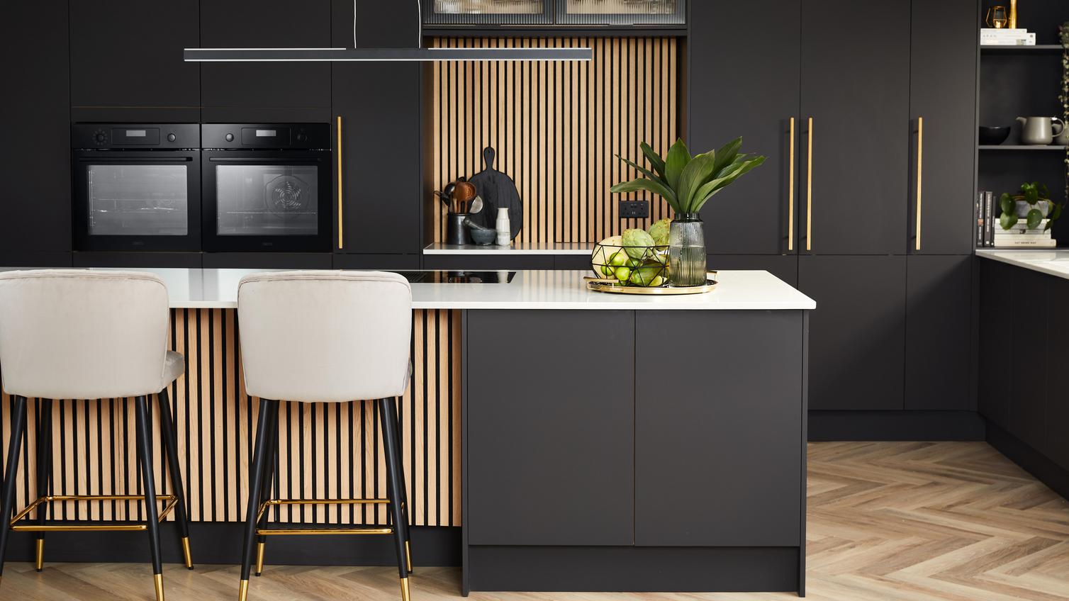 Howdens 2022 Kitchen Of The Year Winner's kitchen featuring black units, brass handles, white worktops, and chevron flooring.