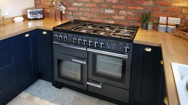 Navy shaker kitchen in a U-shaped layout. Has oak worktops, a slate-grey range cooker, and a chimney extractor.