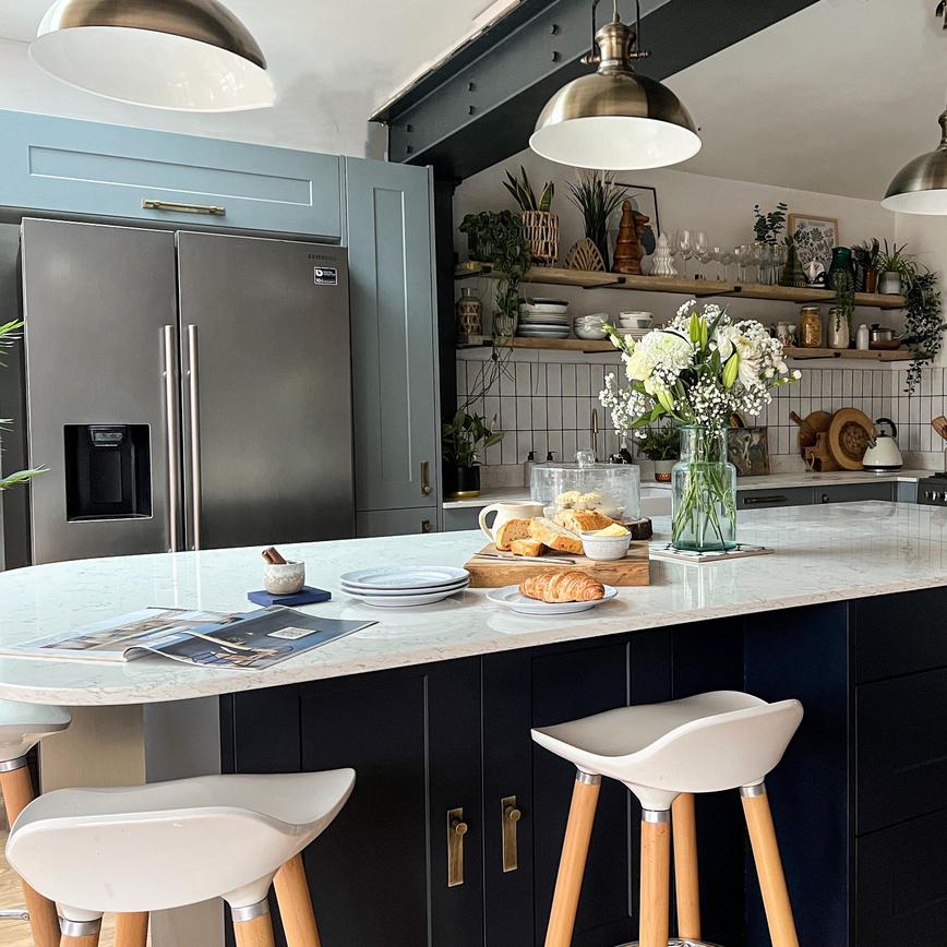 Two-tone shaker kitchen with dusk blue wall units and a navy island, with antique brass handles and white worktops.