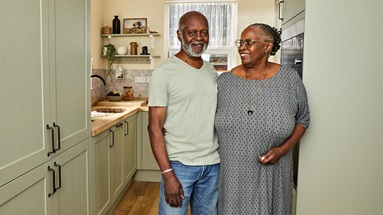Victor and June in their sage green kitchen with shaker doors and a galley layout. Includes timber counters and floors.