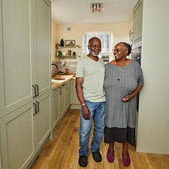 Victor and June in their sage green kitchen with shaker doors and a galley layout. Includes timber counters and floors.