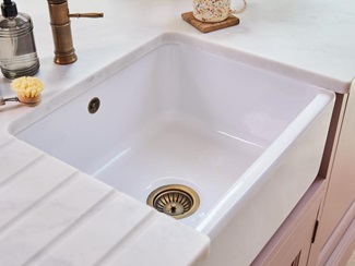 A white worktop with a belfast kitchen sink fitted underneath. The sink has a brass waste and strainer and matching overflow