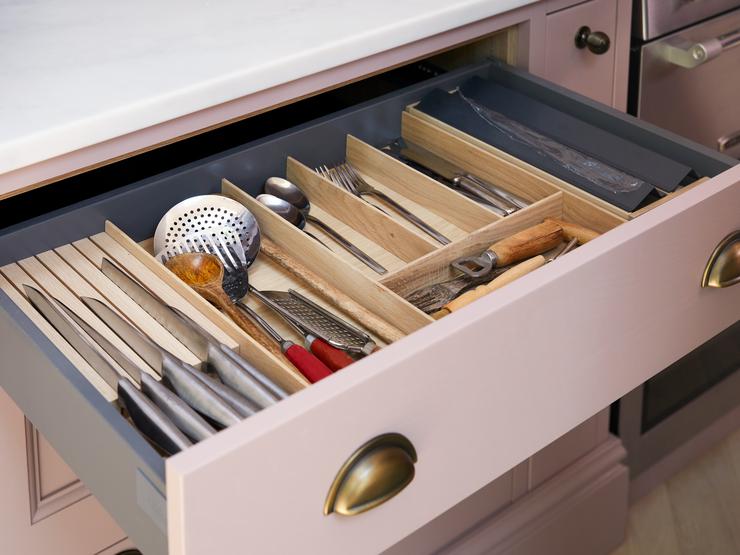 A pink kitchen drawer with brass d-cup handles. Inside is an oak cutlery tray, knife rack, and foil cutter.
