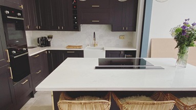 A luxurious black kitchen idea that features an island layout, brass bar handles and taps, and white, square-edge worktops.