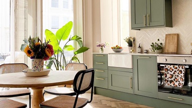 Paintable kitchen design in Victorian room with geen shaker cupboards, chevron flooring, a round table, and open windows.